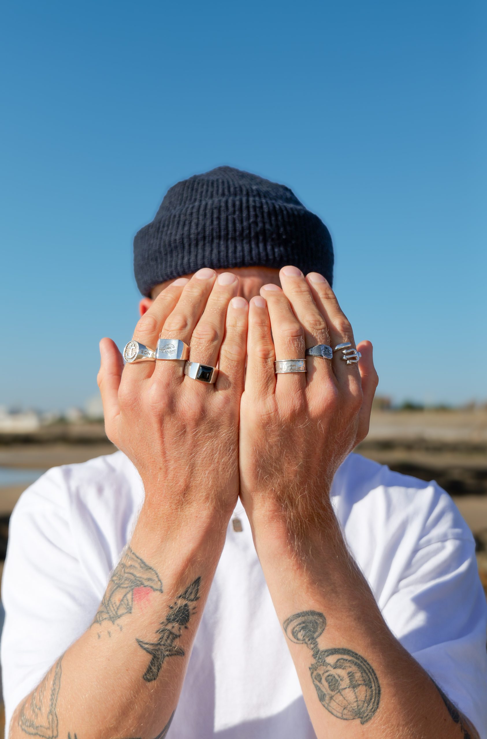 Personne portant plusieurs bagues en argent, les mains devant le visage, lors d’une séance photo pour la marque de bijoux Mr. Salty.