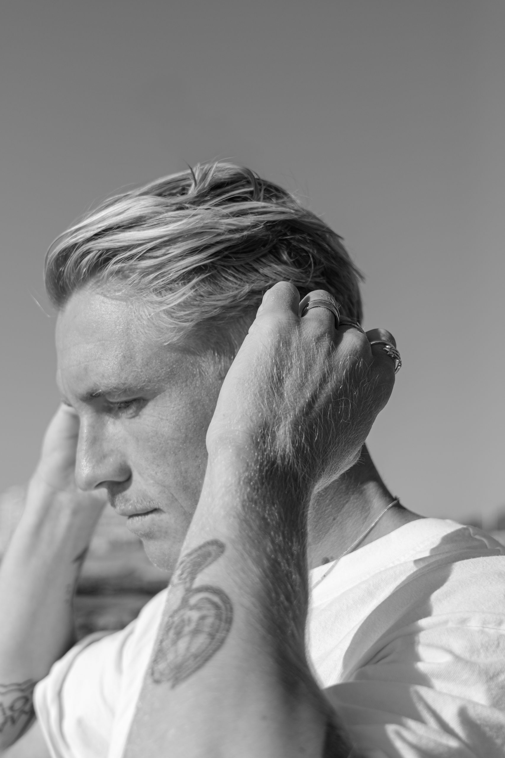 Portrait en noir et blanc d’un homme aux cheveux clairs, photographié de profil dans une lumière naturelle, dans un style artistique et minimaliste.
